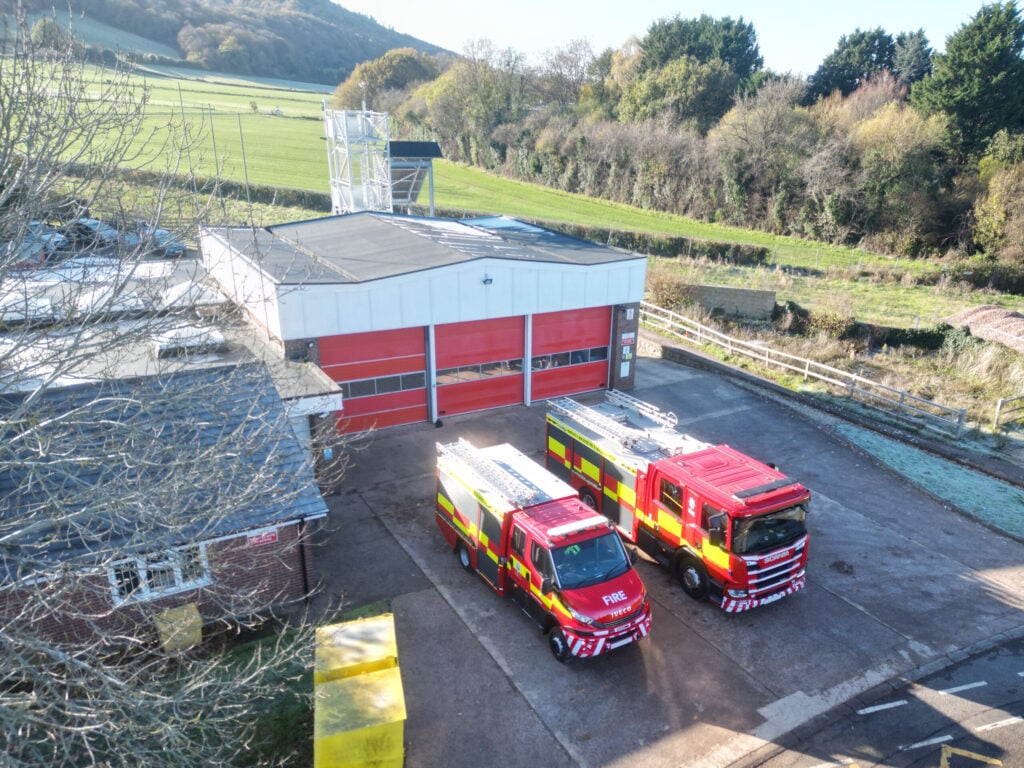 Fire engine and compact fire engine in front of fire station with countryside in background