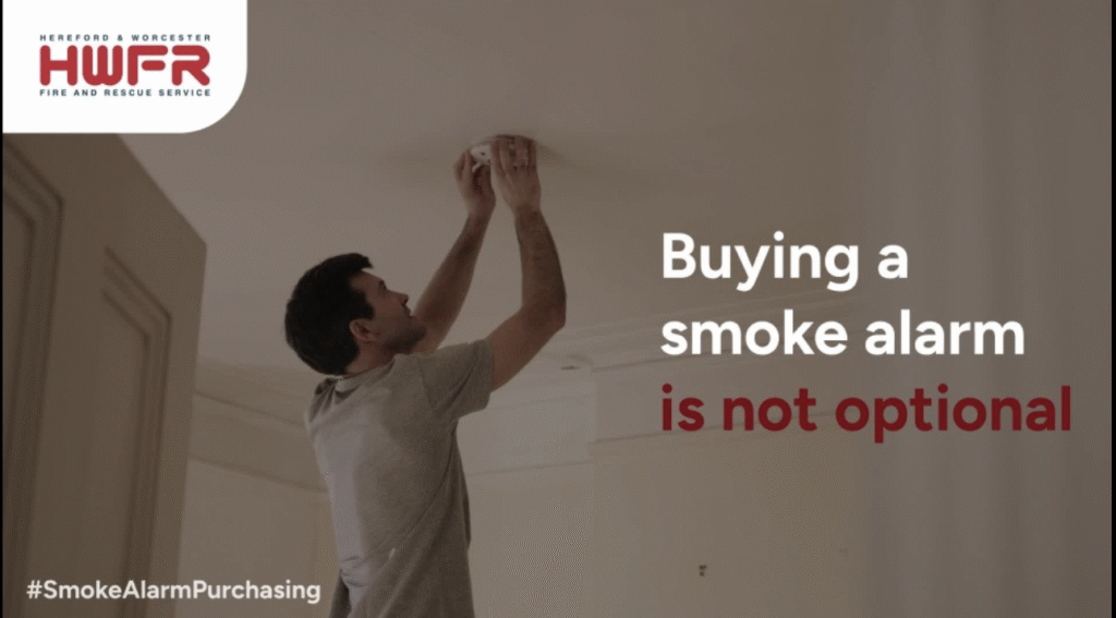 Image of man putting up a smoke alarm, with the words buying a smoke alarm isn't optional next to it. Aimed at Herefordshire and Worcestershire Residents