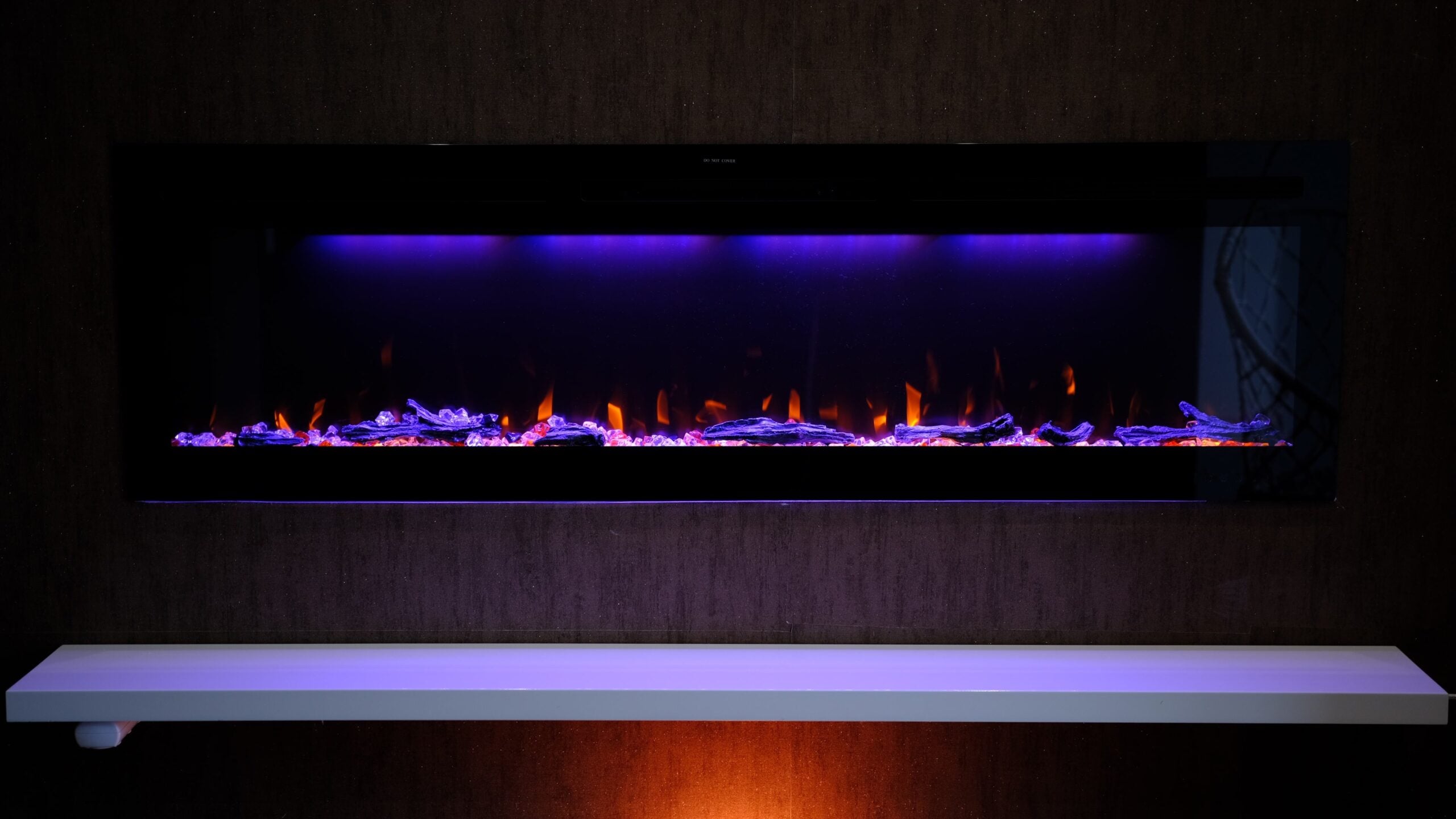 view on electric fireplace with artificial sparkling flame, decor for the interior, orange flame on crystals with orange and purple backlighting.